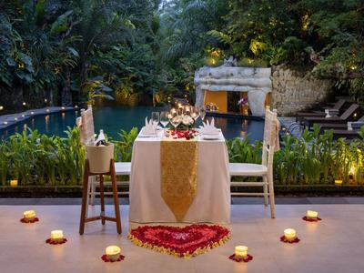 Romantisch diner voor twee met kaarslicht en bloemenversiering bij het water in een tropische omgeving.