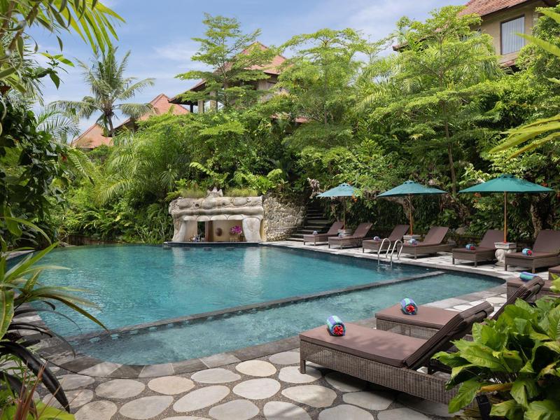 Verwarmd buitenzwembad met ligstoelen en parasols, omringd door weelderig groen.