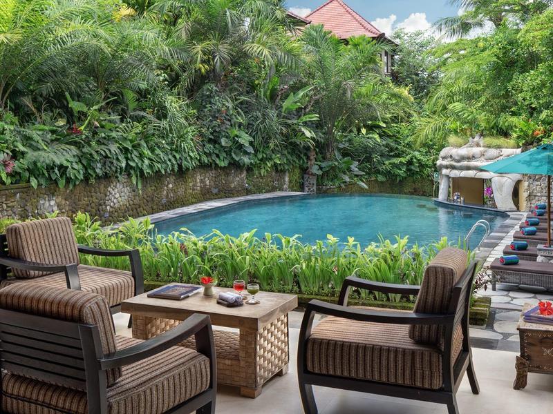 Gezellige zithoek met stoelen en tafel naast een zwembad omgeven door weelderige groene begroeiing.