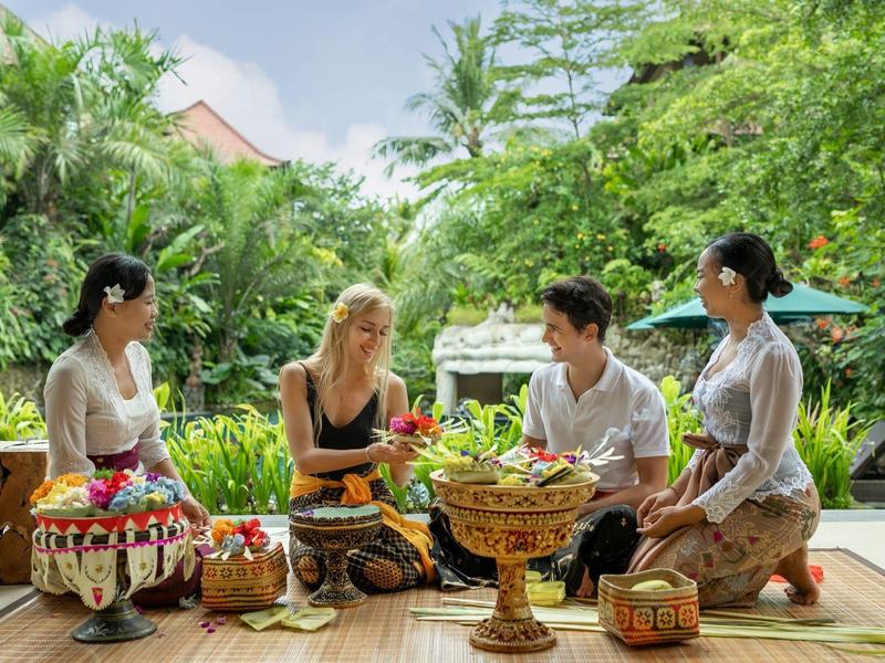 Vier mensen zitten buiten in een tropische omgeving met traditionele manden en versieringen.