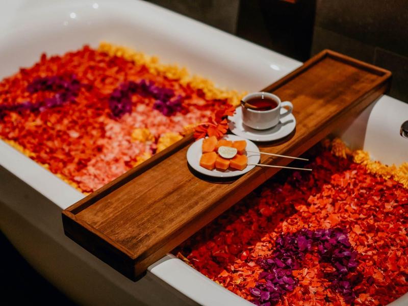 Badkuip gevuld met kleurrijke bloemblaadjes, houten dienblad met koffie en koekjes