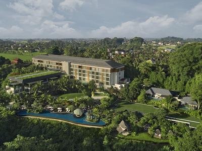 Grand hôtel dans un paysage verdoyant avec piscine et nombreux arbres sous un ciel nuageux.