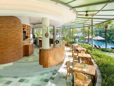 Espace piscine d'hôtel ouvert avec bar et plusieurs tables en bois à côté d'une piscine sous des parasols.
