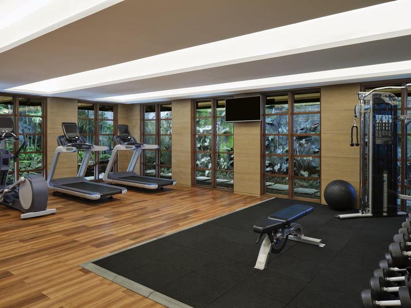 Salle de sport moderne avec tapis de course, poids et banc d'entraînement dans une pièce lumineuse.