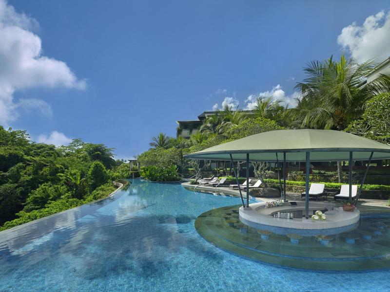 Piscine à débordement avec bar sous toit vert entourée de végétation tropicale sous un ciel bleu.