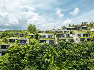 Villas d'hôtel modernes en terrasses entourées d'une végétation dense et verte.