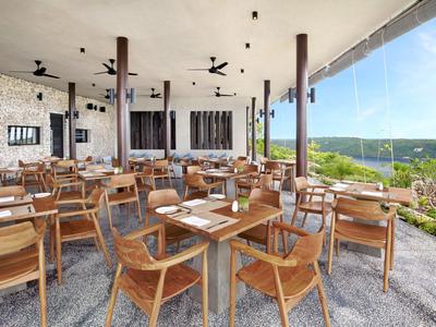 Open-air restaurant with wooden tables and chairs overlooking a green landscape.