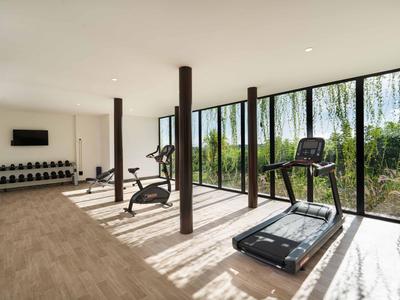 Gym with treadmill, exercise bikes, and large windows overlooking greenery.