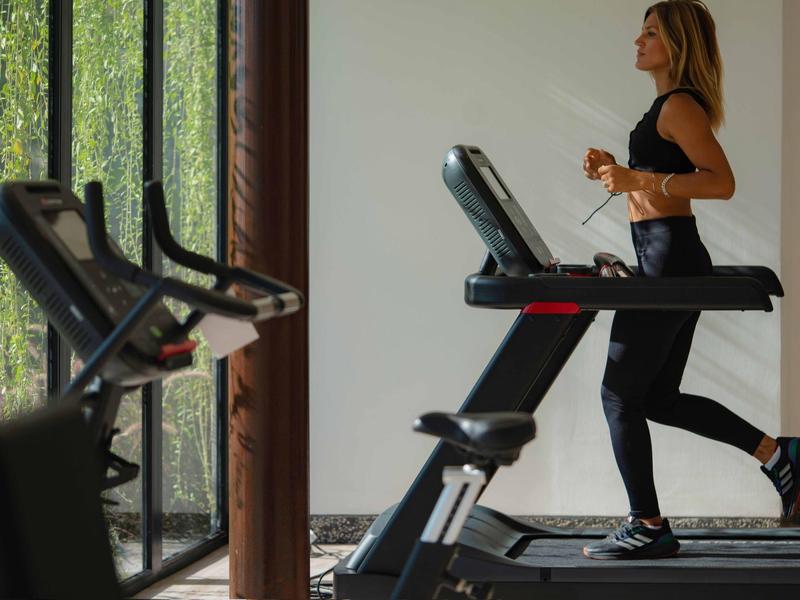 Femme courant sur un tapis roulant dans une salle de sport moderne avec de grandes fenêtres.