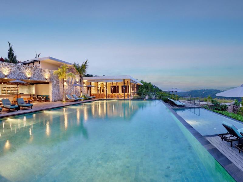 Espace piscine moderne avec chaises longues et vue sur la côte au coucher du soleil.
