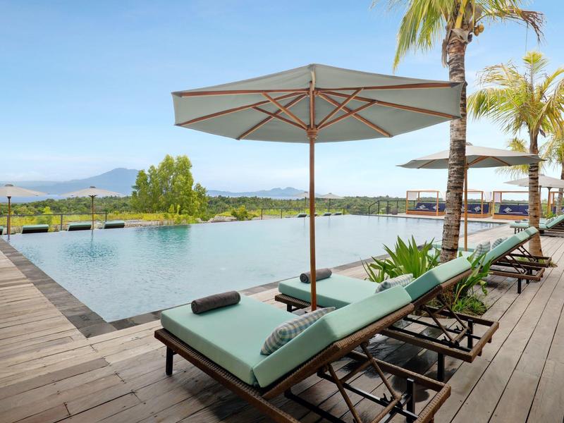 Piscine à débordement extérieure moderne avec chaises longues et parasol sur terrasse en bois.