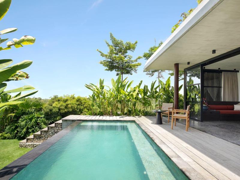 Zone de piscine moderne avec chaises longues à côté d'une chambre ouverte et végétation luxuriante.