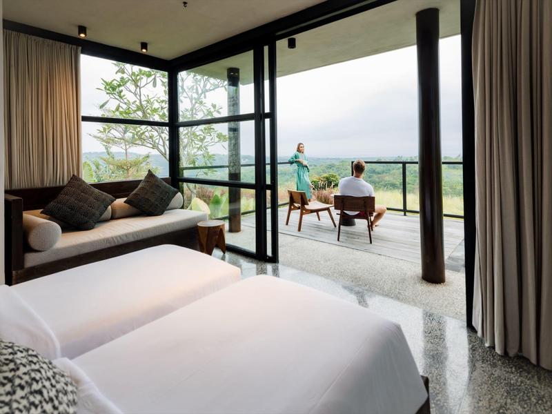 Chambre d'hôtel moderne avec lit, canapé et terrasse ouverte donnant sur la nature.