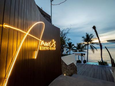 Leuchtschrift "Prawn's" an Holzwand, dahinter Palmen und Meer bei Sonnenuntergang.