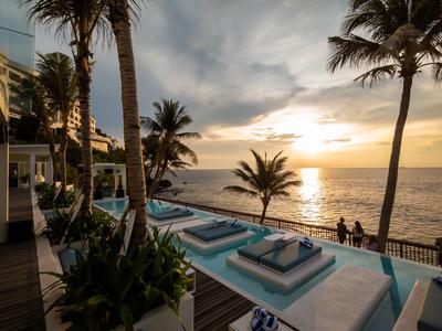 Abendstimmung am Meer mit Poolliegen, Palmen und Sonnenuntergang über dem Ozean.