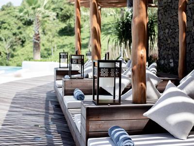 Lounge rilassante con cuscini bianchi e asciugamani accanto a una piscina e un ponte in legno