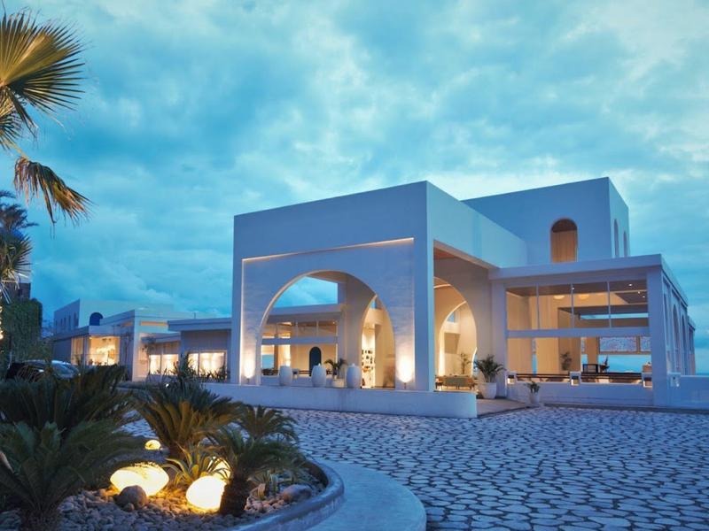 Modernes weißes Gebäude mit klaren Linien, Palmen und blauem Himmel im Hintergrund bei Abenddämmerung.