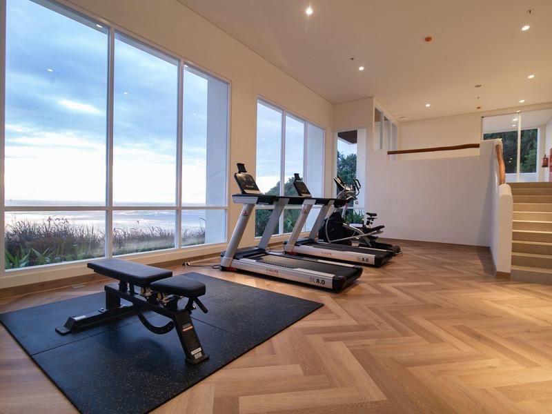 Moderner Fitnessraum mit großen Fenstern, Laufbändern, Hanteln und Holzparkettboden.