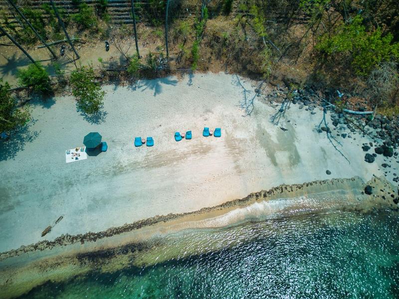 Strand mit weißem Sand, blauem Wasser, Sonnenschirmen und gleichmäßig angeordneten Liegestühlen.
