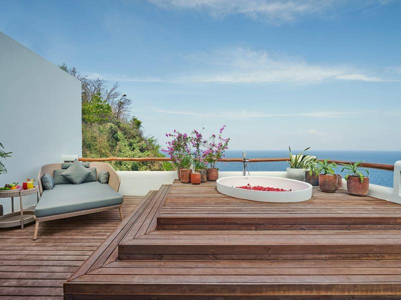 Terrasse mit Holzdeck, Whirlpool, grünen Pflanzen und Meerblick unter blauem Himmel.