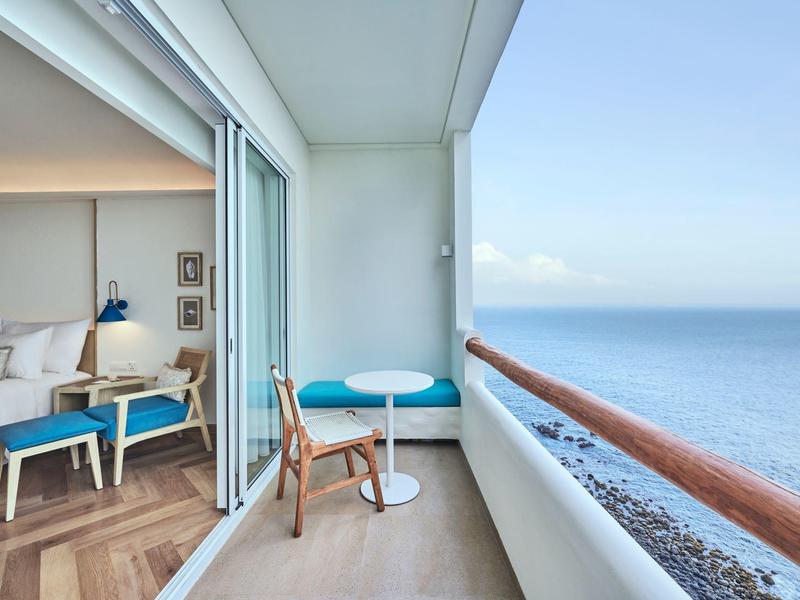 Balkon mit kleinem Tisch, Stuhl und Meerblick, angrenzend an modernes Schlafzimmer mit Holzfußboden.