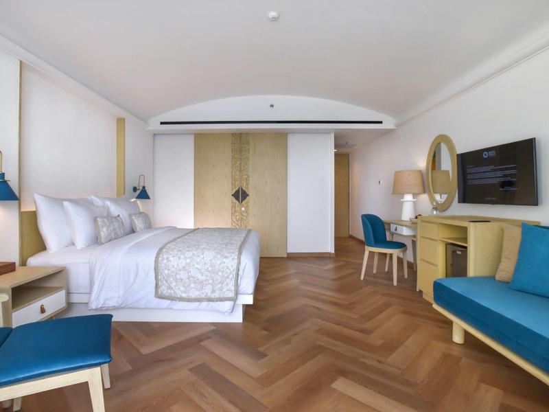 Modernes Hotelzimmer mit Doppelbett, Holzboden, blauem Sofa und Schreibtisch mit Fernseher.