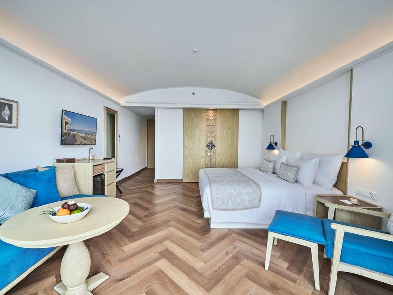 Modernes Hotelzimmer mit Doppelbett, Sitzbereich, blauen Akzenten und Holzfußboden im Fischgrätmuster.