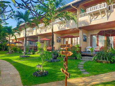Terreno de hotel con césped bien cuidado, plantas exóticas y terraza bajo un cielo azul
