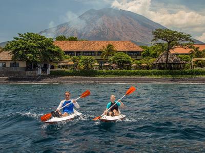 Dos personas practicando kayak en el agua frente a un hotel con montaña al fondo.