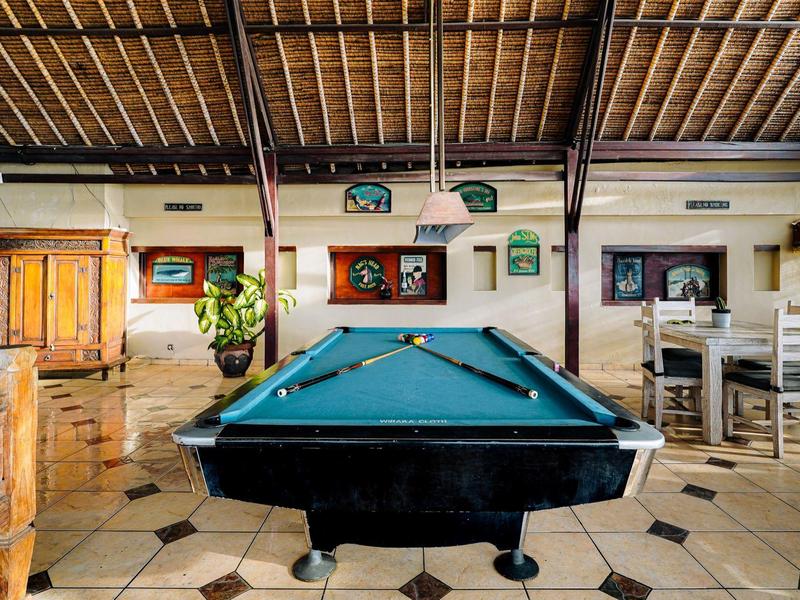 Een pooltafel staat in een rustieke kamer met een houten plafond en betegelde vloer.