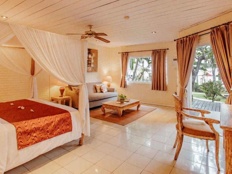 Lichte kamer met hemelbed, zithoek, bureau en uitzicht op bomen.