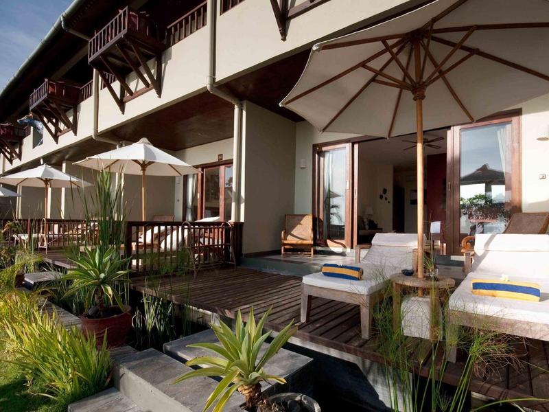 Terras van een hotelkamer met ligstoelen, parasols en tuinmeubilair bij daglicht.