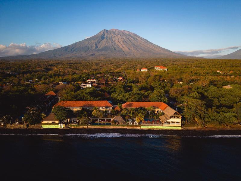 Hotel aan het water met een grote vulkaan op de achtergrond.