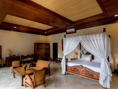 Przestronny pokój hotelowy z łóżkiem z baldachimem, drewnianym sufitem i częścią wypoczynkową z krzesłami i stołem.