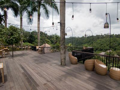 Große Terrasse mit Holzboden, Stühlen und Tischen, umgeben von Palmen und grüner Landschaft.