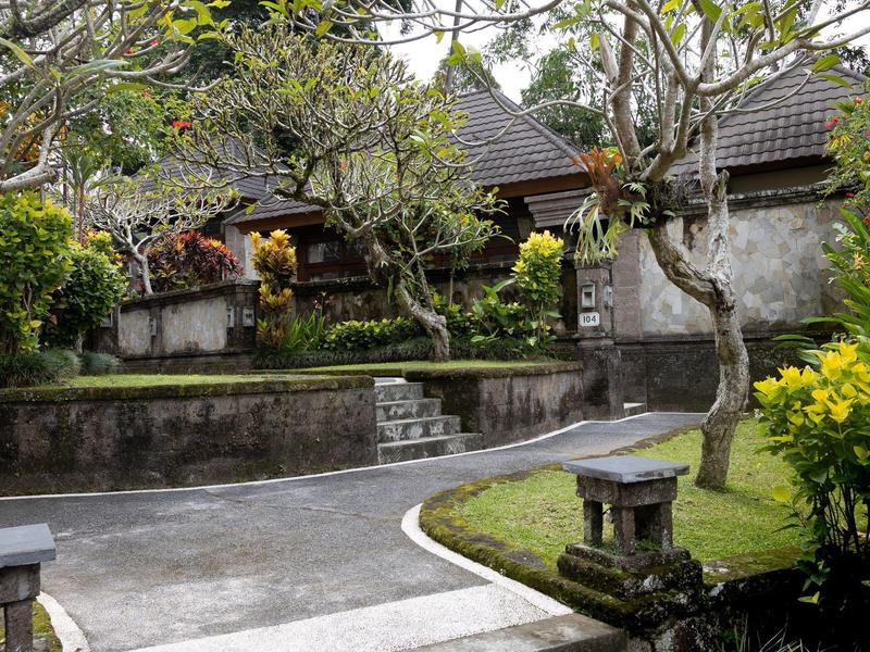 Ścieżka w ogrodzie z drzewami i kamiennymi latarniami przed tradycyjnymi budynkami.