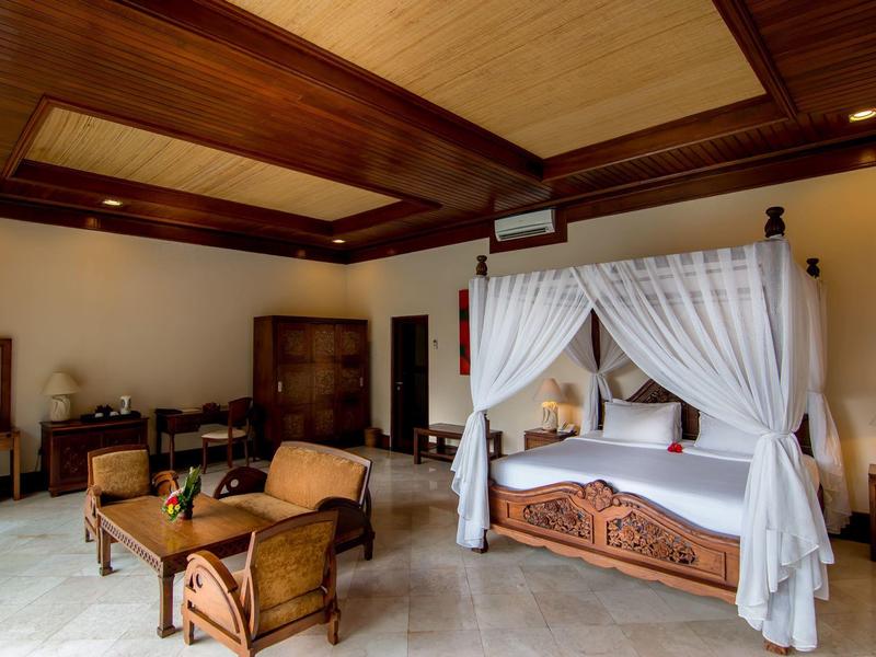 Przestronny pokój hotelowy z łóżkiem z baldachimem, drewnianym sufitem i częścią wypoczynkową z krzesłami i stołem.