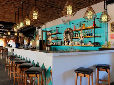 Vista interna di un bar elegante con sgabelli, bancone blu e lampade a sospensione calde.