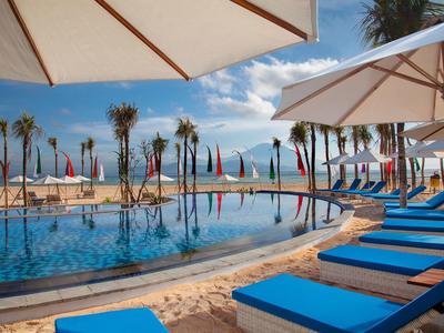 Area piscina di lusso con lettini blu e ombrelloni accanto a palme e vista mare.