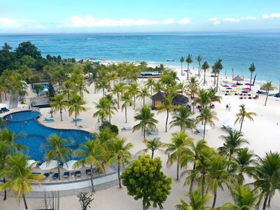 Complesso alberghiero con più piscine, palme e spiaggia di sabbia bianca sul mare.