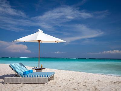 Spiaggia vuota con ombrellone bianco e sdraio vicino al mare turchese sotto un cielo azzurro.