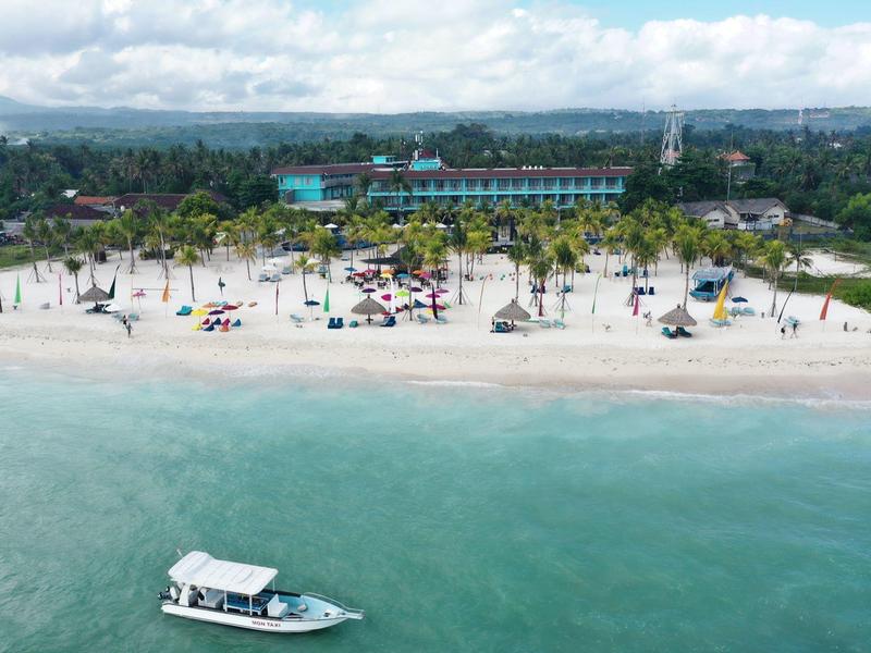 Vista di una spiaggia di sabbia bianca con palme, ombrelloni e una barca in acqua limpida.