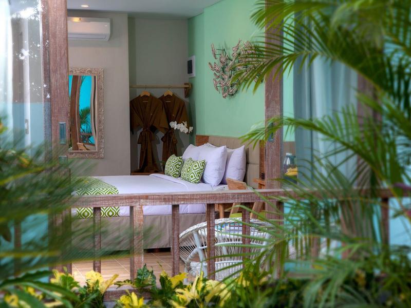 Accogliente balcone dell'hotel con panca di legno, cuscini e vista su piante verdi.