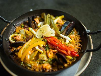 Kolorowa paella z owocami morza, papryką i cytryną na czarnej patelni.