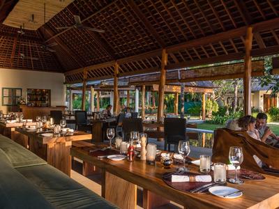 Otwarta restauracja z drewnianymi meblami i widokiem na zielony ogród o zmierzchu.