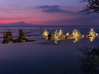 Wieczorny widok na oświetlony basen z morzem i górami w tle.