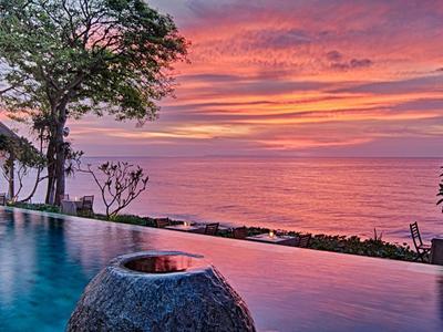 Piscina infinita con vista al atardecer sobre el mar y vegetación tropical