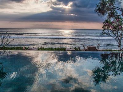 Zachód słońca nad morzem z basenem infinity na pierwszym planie i drzewem na brzegu.