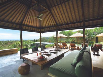 Otwarta zadaszona przestrzeń do siedzenia z widokiem na zielony krajobraz i morze w tle.