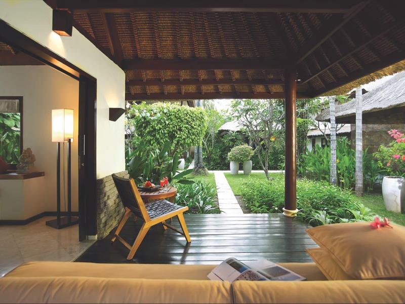 Zadaszony taras z drewnianą podłogą, krzesłami i widokiem na zadbany ogród w hotelu.